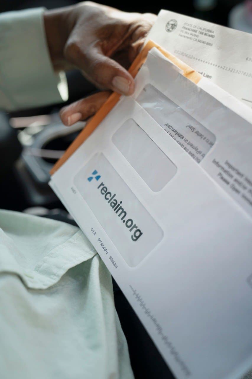 Hand holding a stack of mail topped by a Reclaim.org window envelope
